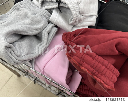 Sweatpants in shades of gray, pink, and red displayed in metal shopping basket in store Sweatpants in shades of gray, pink, and red displayed in metal shopping basket in store 138685818