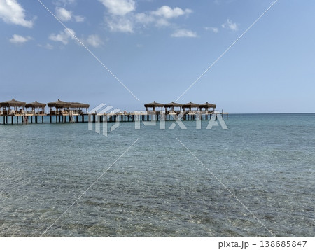 Wooden pier extends over calm sea with straw-roof huts under blue sky, perfect background Wooden pier extends over calm sea with straw-roof huts under blue sky, perfect background 138685847