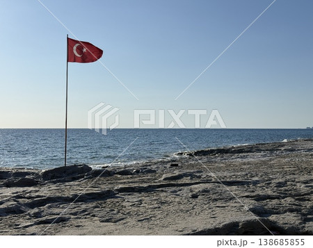 Turkish flag on rocky beach with clear sky background, symbolizing national pride and serenity Turkish flag on rocky beach with clear sky background, symbolizing national pride and serenity 138685855