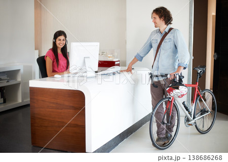 Office, desk and man with bike for business, travel and talking about commute to work with receptionist in morning. Businessman, bicycle and conversation with woman in administration or secretary 138686268