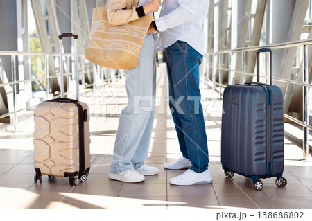 Closeup of mature couples legs standing together in airport corridor with suitcases Closeup of mature couples legs standing together in airport corridor with suitcases 138686802