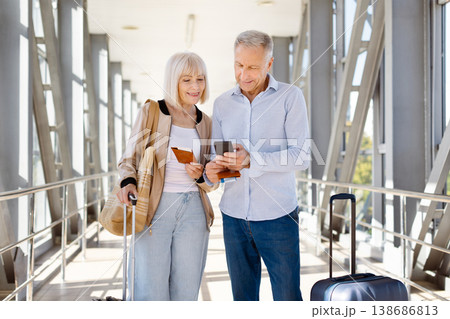Mature couple standing in airport, man using smartphone while woman holds passport Mature couple standing in airport, man using smartphone while woman holds passport 138686813