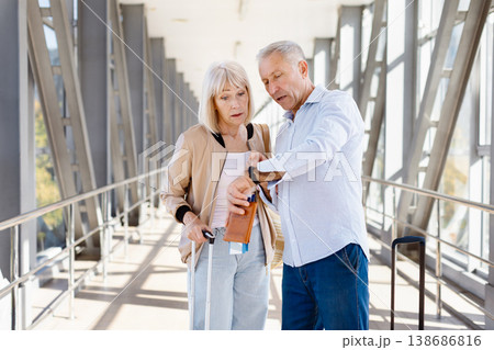 Mature couple at airport terminal checking time and travel documents Mature couple at airport terminal checking time and travel documents 138686816