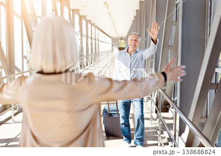 Mature couple meeting at airport terminal, smiling and waving with luggage 138686824
