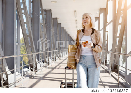 Mature woman walking alone in airport terminal with luggage and passport Mature woman walking alone in airport terminal with luggage and passport 138686827