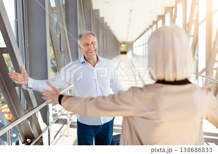 Mature couple meeting in sunlit airport corridor after plane arrival Mature couple meeting in sunlit airport corridor after plane arrival 138686833
