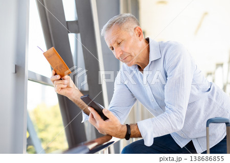 Mature man holding passport and smartphone in airport, checking travel information Mature man holding passport and smartphone in airport, checking travel information 138686855