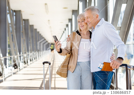 Mature couple leaning on airport railing looking at smartphone together Mature couple leaning on airport railing looking at smartphone together 138686857