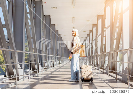Mature woman standing in airport terminal with suitcase and passport, looking back 138686875