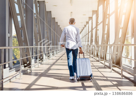 Mature man walking away in airport terminal pulling suitcase, rear view 138686886