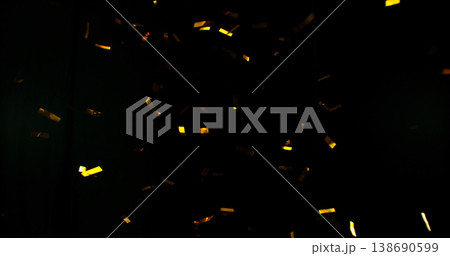 Flying golden confetti on black background. Shiny particles suspended in the air with dramatic lighting, creating a festive, luxury and celebratory atmosphere. 138690599