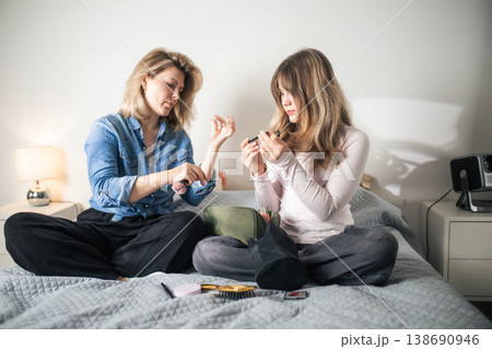 Women sharing makeup routine on bed Women sharing makeup routine on bed 138690946