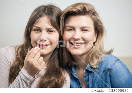 Mother and daughter applying lip gloss, sharing beauty moment 138690983