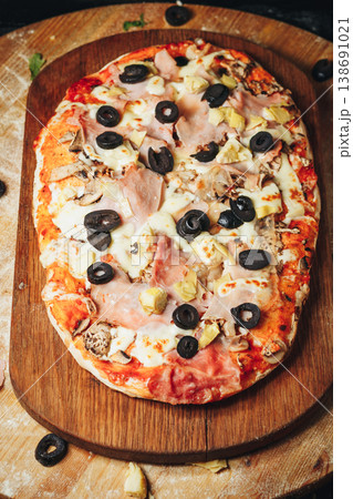 Traditional Italian pinsa romana capricciosa topped with tomato sauce mozzarella ham black olives artichokes and mushrooms on a wooden board. Traditional Italian pinsa romana capricciosa topped with tomato sauce mozzarella ham black olives artichokes and mushrooms on a wooden board. 138691021