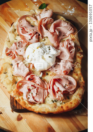 Traditional Italian pinsa romana topped with thin slices of mortadella, creamy burrata cheese and crushed pistachios on a wooden board. Traditional Italian pinsa romana topped with thin slices of mortadella, creamy burrata cheese and crushed pistachios on a wooden board. 138691057
