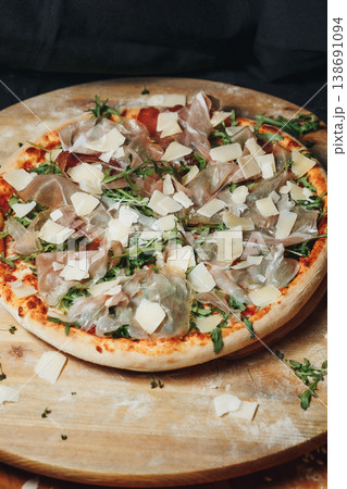 Traditional Italian pizza topped with fresh arugula savory prosciutto ham and generous parmesan shavings served on a rustic wooden board. 138691094