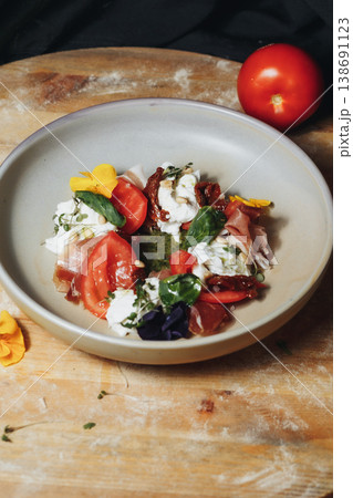 Gourmet Italian Caprese salad with fresh burrata cheese prosciutto ham cherry tomatoes and pesto sauce garnished with edible flowers. Gourmet Italian Caprese salad with fresh burrata cheese prosciutto ham cherry tomatoes and pesto sauce garnished with edible flowers. 138691123