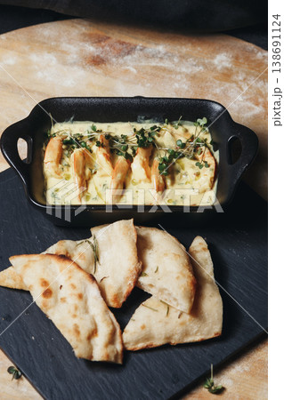 Gourmet shrimps in creamy garlic sauce garnished with fresh microgreens served in a black ceramic dish with toasted flatbread. 138691124