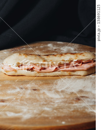 Traditional Italian piadina sandwich filled with thin slices of mortadella ham and creamy cheese served on a rustic floured wooden board. Traditional Italian piadina sandwich filled with thin slices of mortadella ham and creamy cheese served on a rustic floured wooden board. 138691125