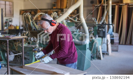 Experienced carpenter measuring wood in woodworking workshop 138692194