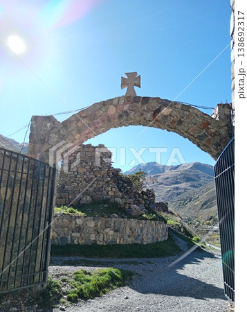 Stone Alan Monastery, North Ossetia, Russia, bright summer day. Ancient stone walls and towers of the medieval Christian complex in a green mountain valley Stone Alan Monastery, North Ossetia, Russia, bright summer day. Ancient stone walls and towers of the medieval Christian complex in a green mountain valley 138692317