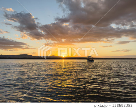 Sunset over water with boat in distance during evening hours Sunset over water with boat in distance during evening hours 138692382