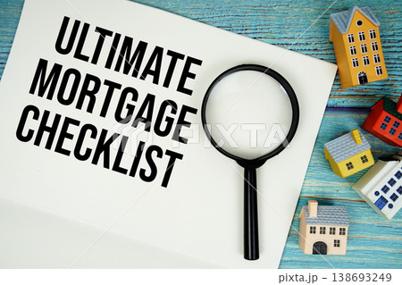 Notepad with "Ultimate Mortgage Checklist" with magnifying glass and house model on wooden background 138693249