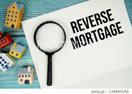 Notepad with "Reverse Mortgage" with magnifying glass and house model on wooden background Notepad with "Reverse Mortgage" with magnifying glass and house model on wooden background 138693268