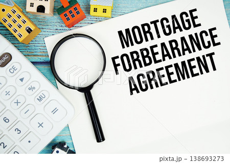 Notepad with "Mortgage Forbearance Agreement" with Calculator, magnifying glass and house model on wooden background 138693273
