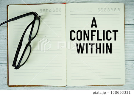Notepad with message "A Conflict Within" and eyeglass on wooden background 138693331