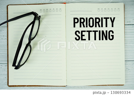 Notepad with message "Priority Setting" and eyeglass on wooden background Notepad with message "Priority Setting" and eyeglass on wooden background 138693334