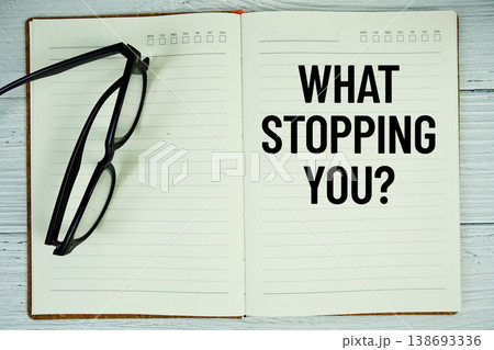 Notepad with message "What Stopping You?" and eyeglass on wooden background 138693336