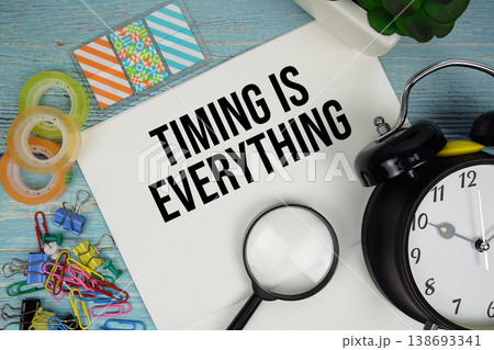 Timing is Everything text on a paper surrounded by office supplies, a magnifying glass, and a clock on a blue wooden surface Timing is Everything text on a paper surrounded by office supplies, a magnifying glass, and a clock on a blue wooden surface 138693341