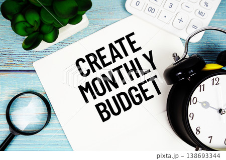 Create Monthly Budget message written on paper placed on a blue wooden surface, alongside a magnifying glass, a clock, a calculator, and a small plant Create Monthly Budget message written on paper placed on a blue wooden surface, alongside a magnifying glass, a clock, a calculator, and a small plant 138693344