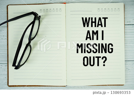 Notepad with message "What Am I Missing Out?" and eyeglass on wooden background 138693353
