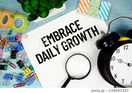 Embrace Daily Growth text on a paper surrounded by office supplies, a magnifying glass, and a clock on a blue wooden surface Embrace Daily Growth text on a paper surrounded by office supplies, a magnifying glass, and a clock on a blue wooden surface 138693387