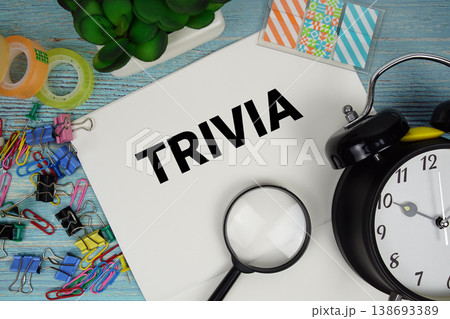 Trivia text on a paper surrounded by office supplies, a magnifying glass, and a clock on a blue wooden surface Trivia text on a paper surrounded by office supplies, a magnifying glass, and a clock on a blue wooden surface 138693389