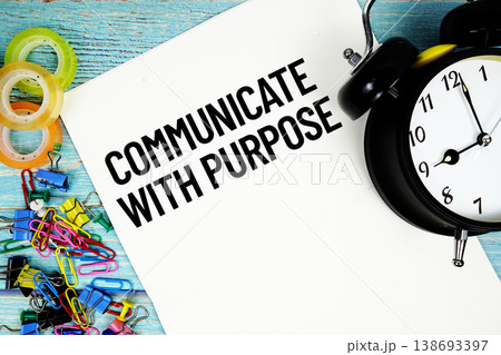 Communicate With Purpose text on a paper surrounded by office supplies and a clock on a blue wooden surface 138693397