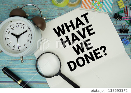 What Have We Done? text on a paper surrounded by office supplies, a magnifying glass, and a clock on a blue wooden surface What Have We Done? text on a paper surrounded by office supplies, a magnifying glass, and a clock on a blue wooden surface 138693572