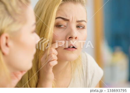 Woman looking at her skin in mirror 138693795