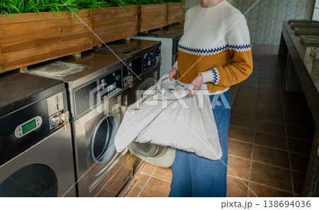Woman loading laundry into washing machine at modern self service laundromat interior lifestyle scene 138694036