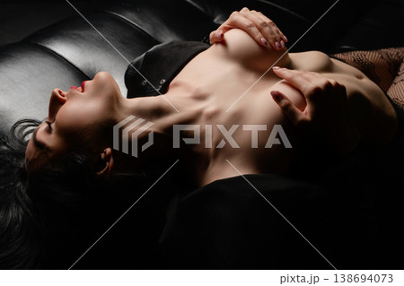 Sensual woman with red lips lying back in a passionate pose on black leather. Sensual woman with red lips lying back in a passionate pose on black leather. 138694073