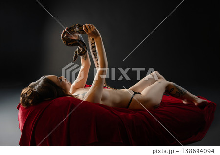 Tattooed Woman in Lingerie Holding a Snake on Red Velvet 138694094