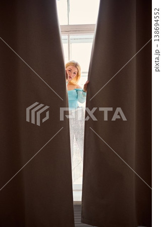 Woman observes street scene through window with curiosity Woman observes street scene through window with curiosity 138694552