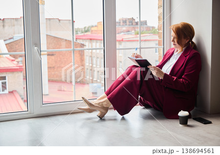 Consultant in burgundy attire prepares for evening reflections by window Consultant in burgundy attire prepares for evening reflections by window 138694561