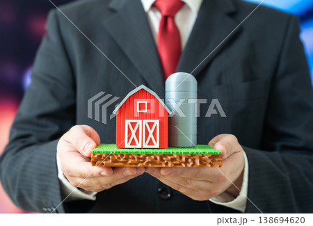 A businessman holds a farm with a plot of land in his hands. Agribusiness and farming. Investment in agriculture supports food production, land ownership and rural economic development. A businessman holds a farm with a plot of land in his hands. Agribusiness and farming. Investment in agriculture supports food production, land ownership and rural economic development. 138694620