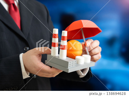 A businessman holds an umbrella over an industrial factory. Insurance and protection of industry and business. Risk management safeguards assets and ensures stability in uncertain conditions. A businessman holds an umbrella over an industrial factory. Insurance and protection of industry and business. Risk management safeguards assets and ensures stability in uncertain conditions. 138694628