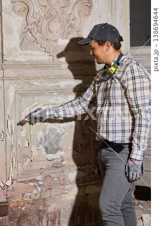 Craftsman in protective gear inspects decorative wall damage carefully 138694644