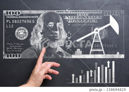 A woman's hand points to a drawn chart and a hundred-dollar bill, symbolizing an analysis of the economy, the oil sector, and financial markets. A woman's hand points to a drawn chart and a hundred-dollar bill, symbolizing an analysis of the economy, the oil sector, and financial markets. 138694829
