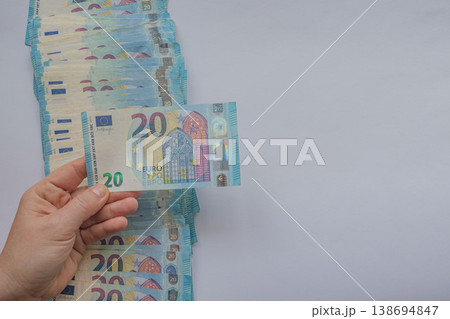Female hand picking a 20 Euro note from a scattered stack on a white background. Minimalist financial layout with vibrant blue currency and large copy space 138694847